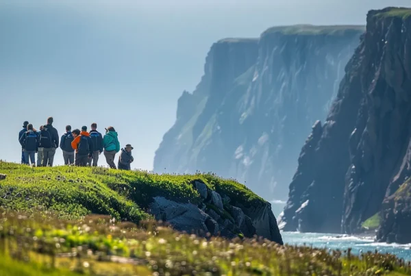 an adventurous wildlife tour group, equipped with high-powered binoculars, observes a majestic grizzly bear foraging along the rugged coastline of alaska’s pristine wilderness, framed by dramatic cliffs and glistening ocean waters.